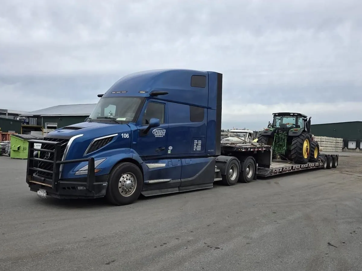 Blue Speedgo Transport truck hauling a farm tractor on a double drop trailer