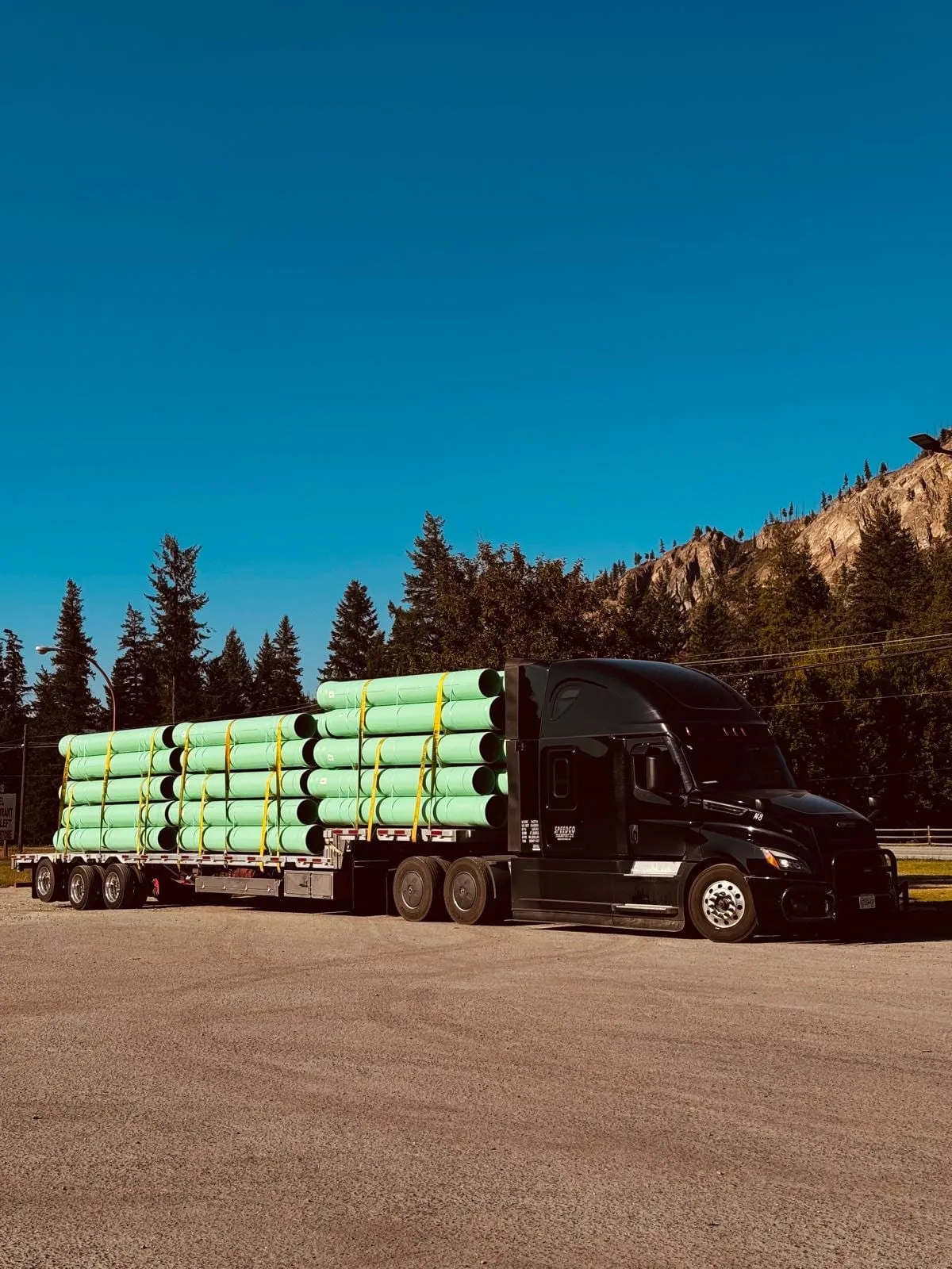 Black Speedgo Transport truck hauling green PVC pipe on a flatbed in the mountains