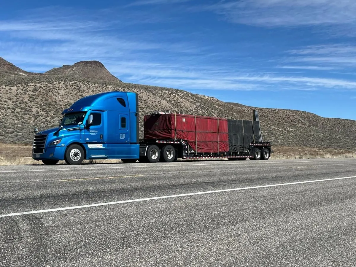 Blue Speedgo Transport truck hauling a tarped step deck load on a desert highway