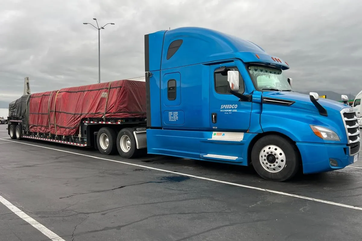 Blue Speedgo Transport truck hauling a full tarped load on a step deck trailer