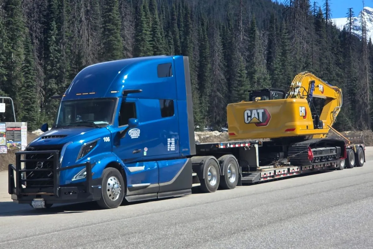 Blue Speedgo Transport truck hauling a CAT excavator on a lowbed trailer