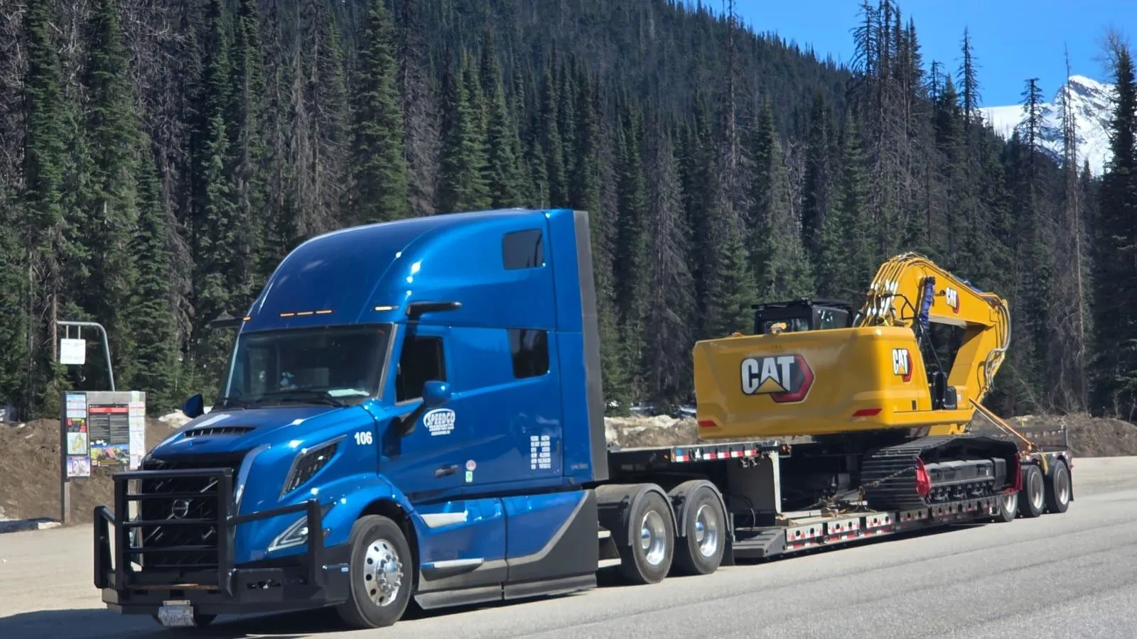 Blue Speedgo Transport truck hauling a CAT excavator on a lowbed trailer