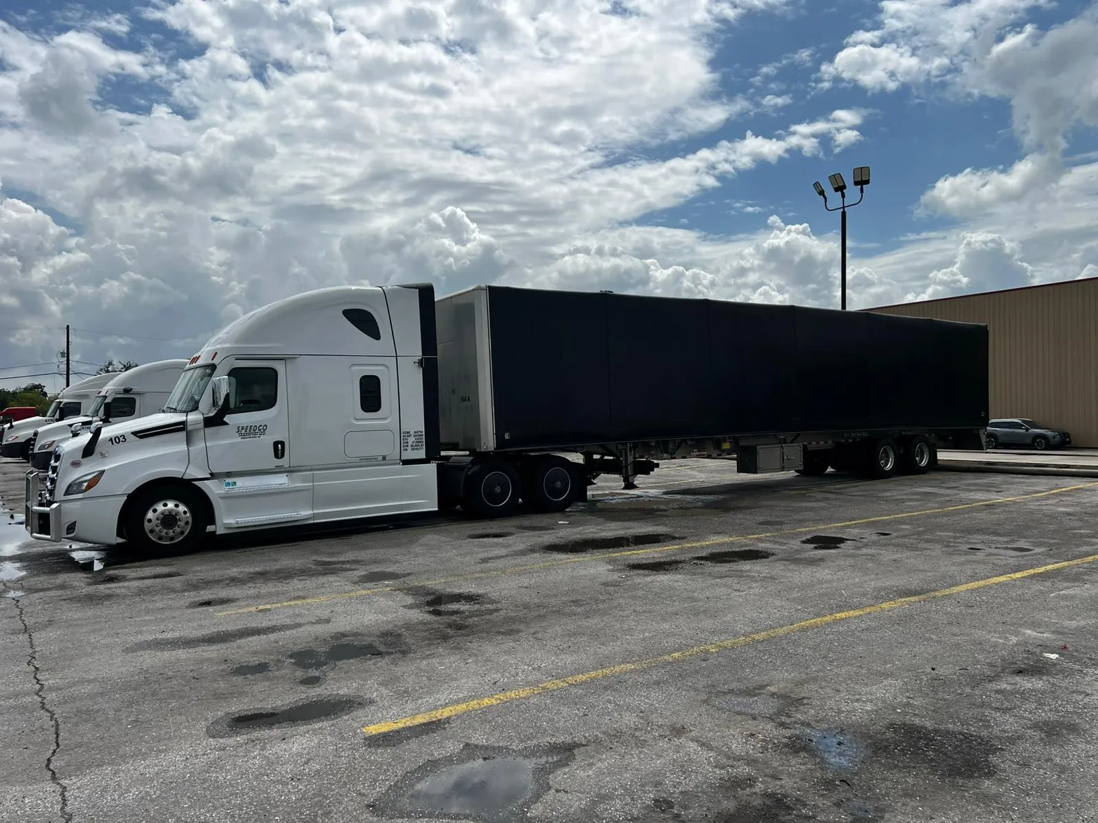 White Speedgo Transport truck pulling a 53' flat deck Conestoga trailer