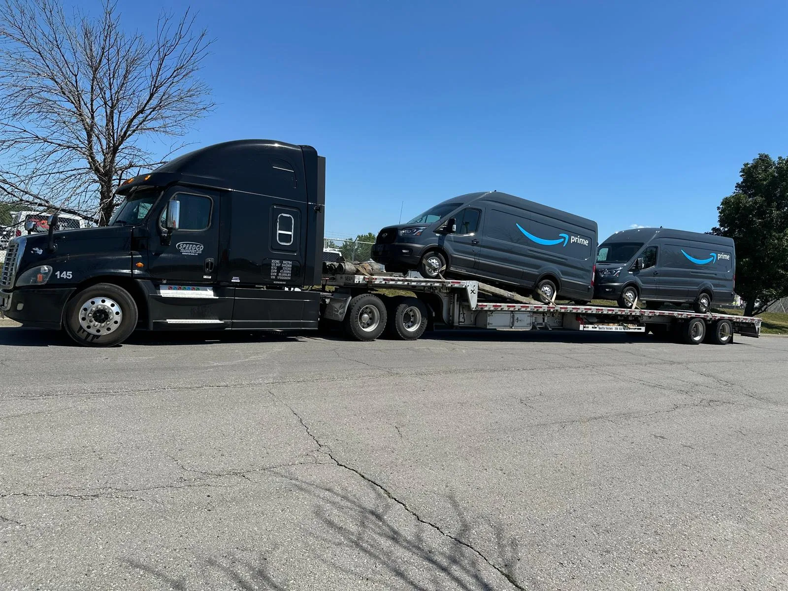Black Speedgo Transport truck hauling two delivery vans on a tandem step deck trailer