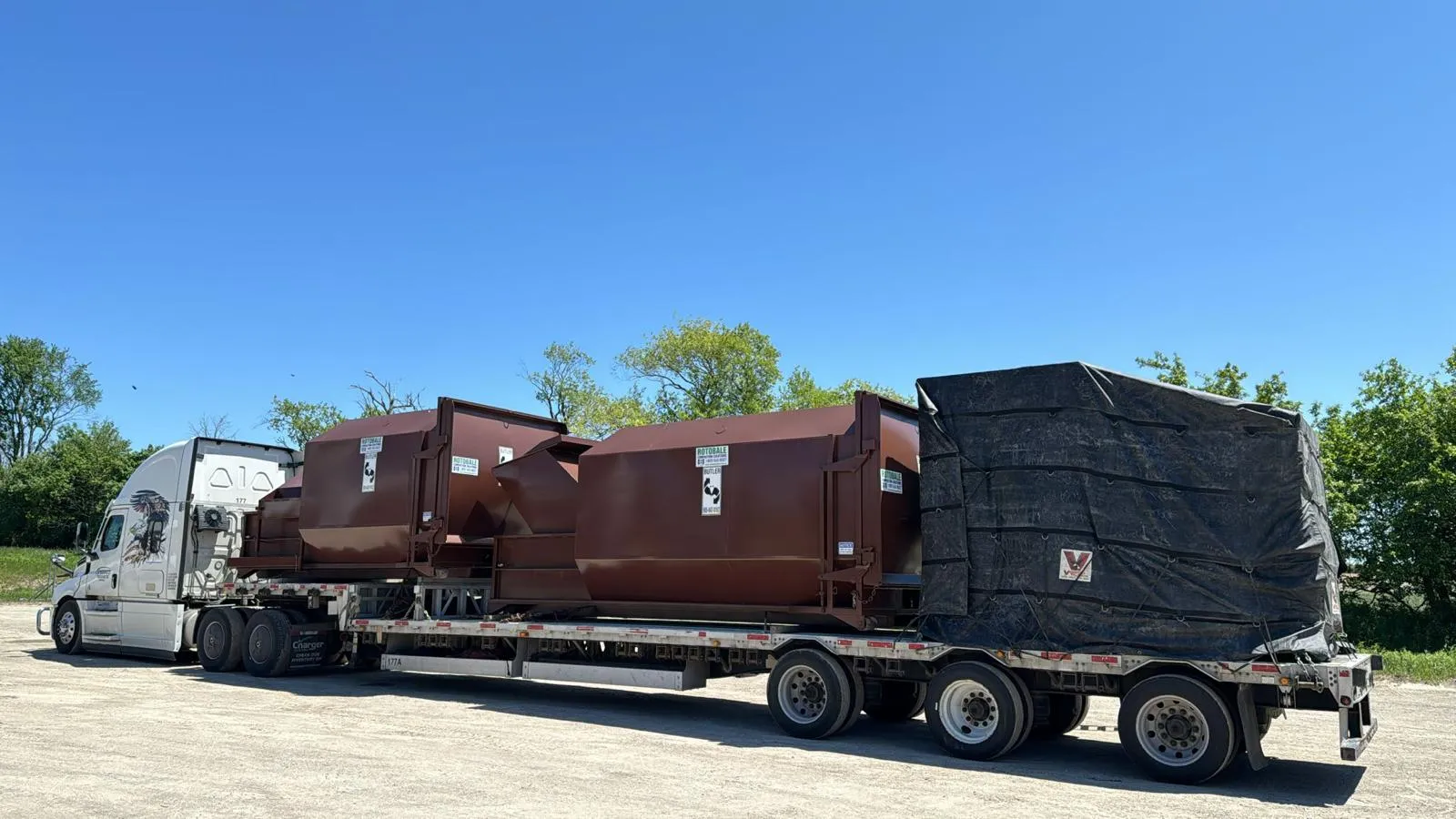 White Speedgo Transport truck hauling steel equipment on a tri-axle step deck trailer