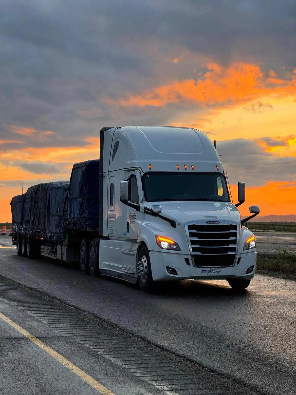 White Speedgo Transport truck hauling a tarped load at sunset